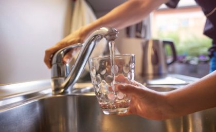 Image: Adobe. A close up a hand turning on a kitchen tap, filling a glass with water.